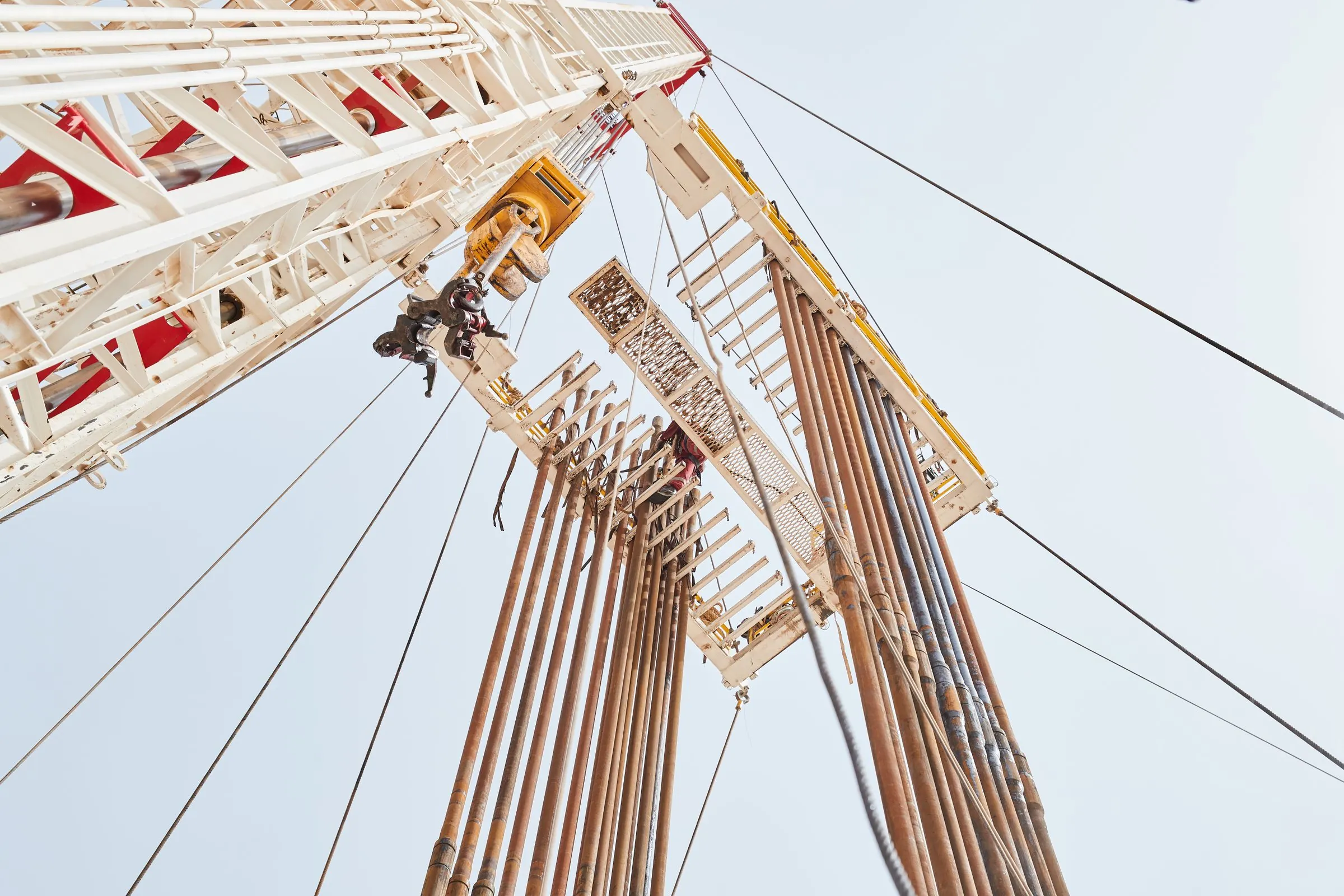 Looking up the mast of a land drilling rig against a pale sky